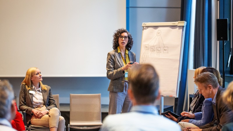 Stock photo of professional learning. A woman presents in front of an easel with various people sitting in chairs around her.